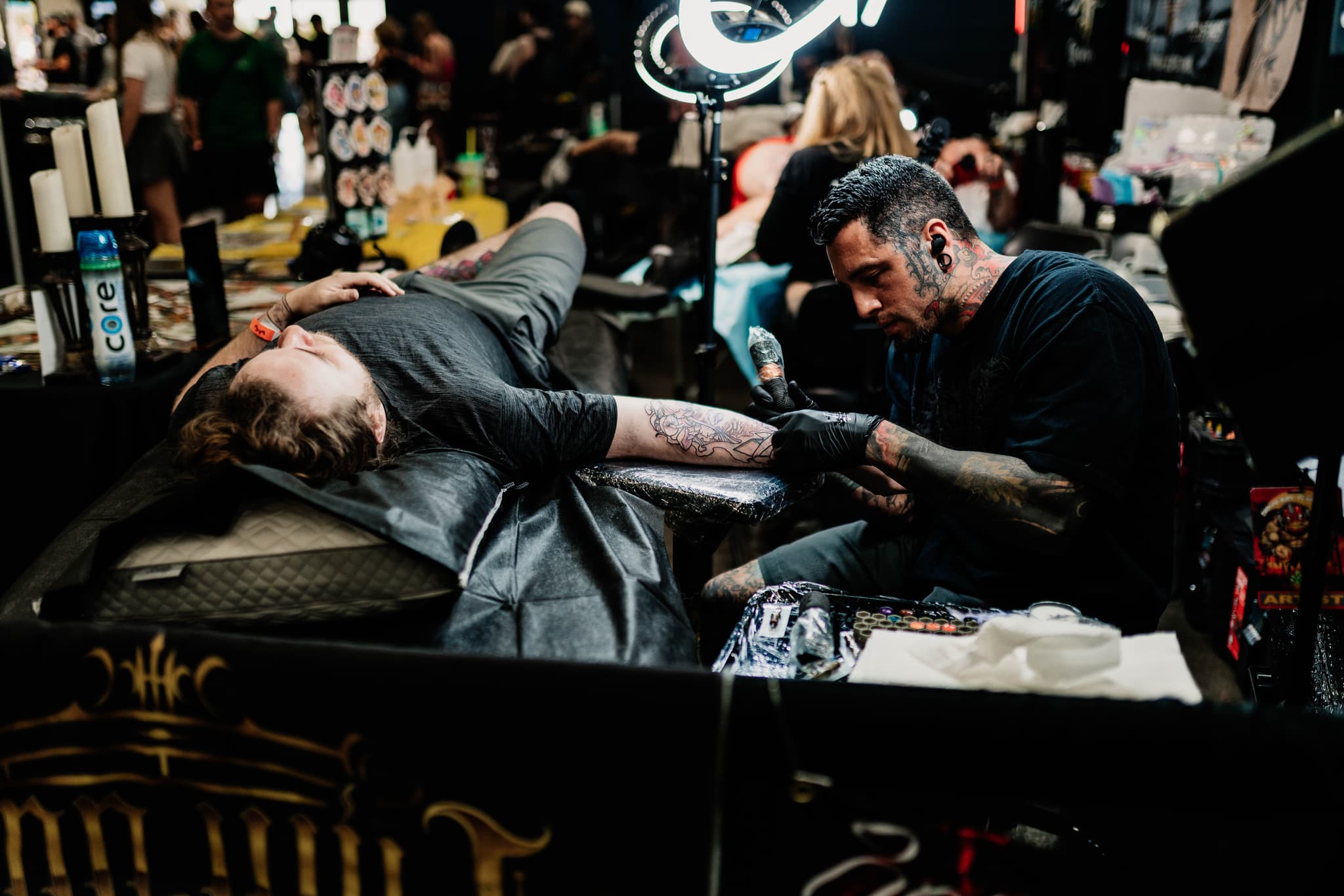 Tattoo artist working on client's arm with tattoo machine and inks — tattoo shop supplies visible.